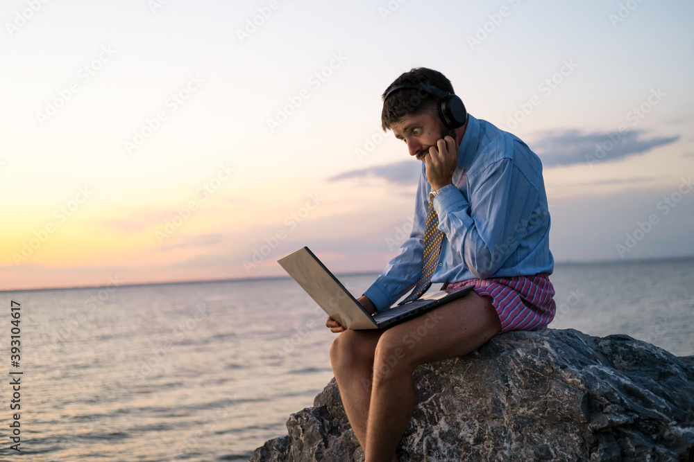 manager works remotely on the seashore at sunset. He is wearing a shirt with a tie, underpants. He experiences the emotion of surprise. Stay home and quarantined.