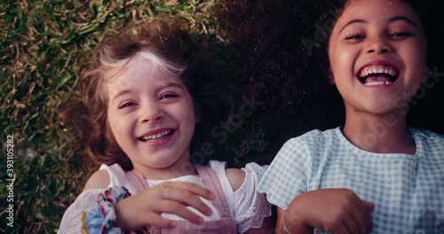 Two happy little girls smiling lying on grass being tickled