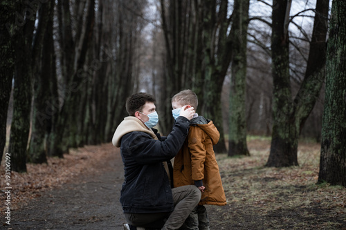 one parent puts on a medical mask on a young son, a young dad walks with his son in the park, winter park, autumn truancy, unconventional family