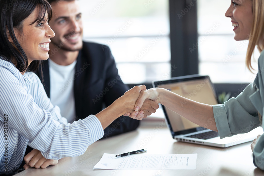 Attractive real-estate agent shaking hands with young couple after signing agreement contract in the office. Attractive real-estate agent shaking hands with young couple after signing agreement contract in the office.