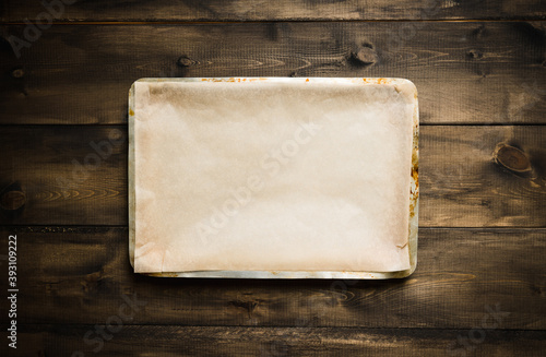 Clean baking sheet with cooking paper on the rustic background. Selective focus. Shot from above. 