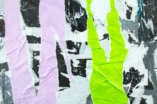 Torn and crumpled purple and green posters glued on billboard with old dirty paper. Abstract and creative background of ripped magazine paper.