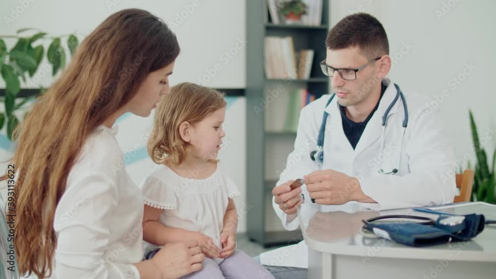 Male Doctor Pediatrician Giving Some Tablets for Ill Kid. Mother With Kid at Visiting Pediatrician. Talking With a Doctor at Consultation During an Appointment. Male Doctor Pediatrician Giving Some Tablets for Ill Kid. Mother With Kid at Visiting Pediatrician. Talking With a Doctor at Consultation During an Appointment.