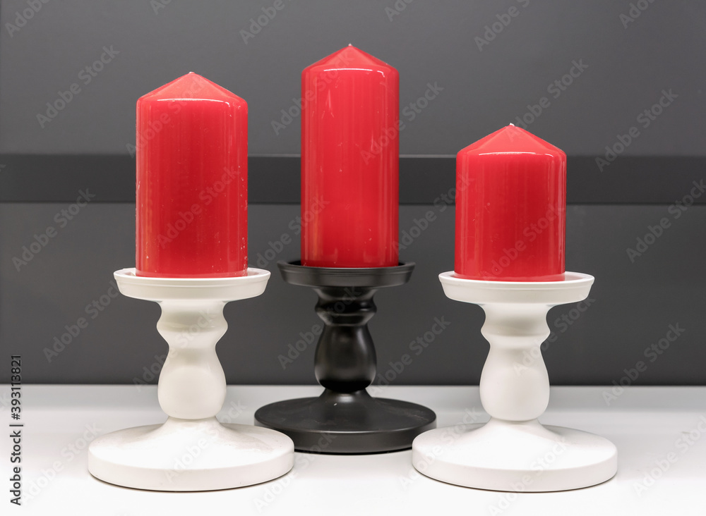 Red Christmas candles in white and black candlesticks on a gray background.