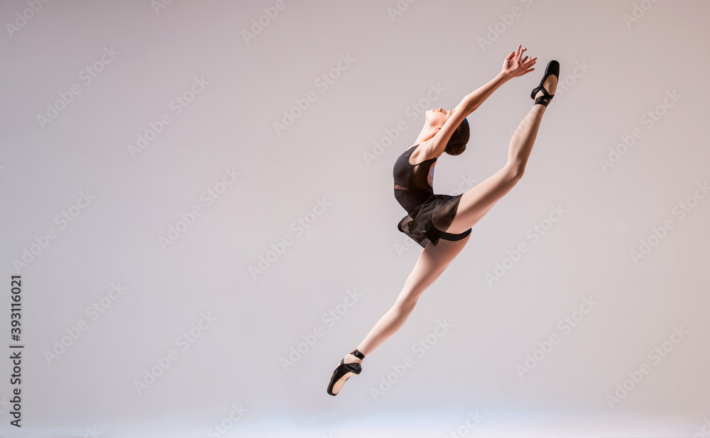 A young ballerina in a black swimsuit and pointes jumps against a bright background. A young ballerina in a black swimsuit and pointes jumps against a bright background.