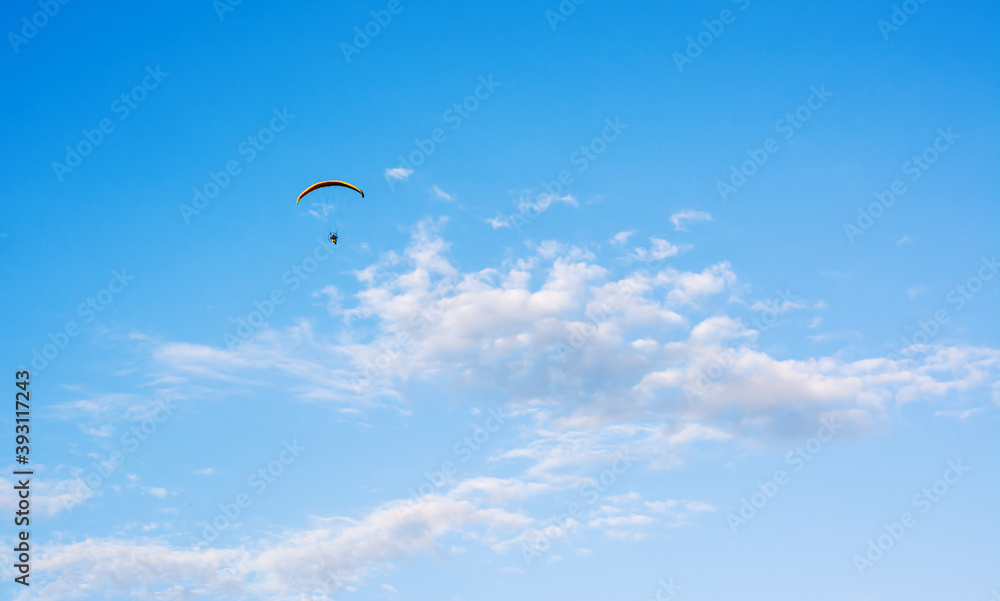 Paraglider flying against blue sky with clouds in middle at sunny daylight Paraglider flying against blue sky with clouds in middle at sunny daylight