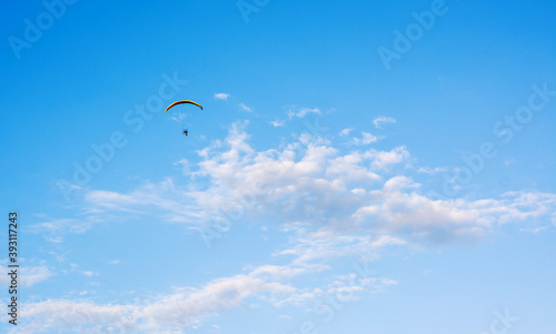 Paraglider flying against blue sky with clouds in middle at sunny daylight