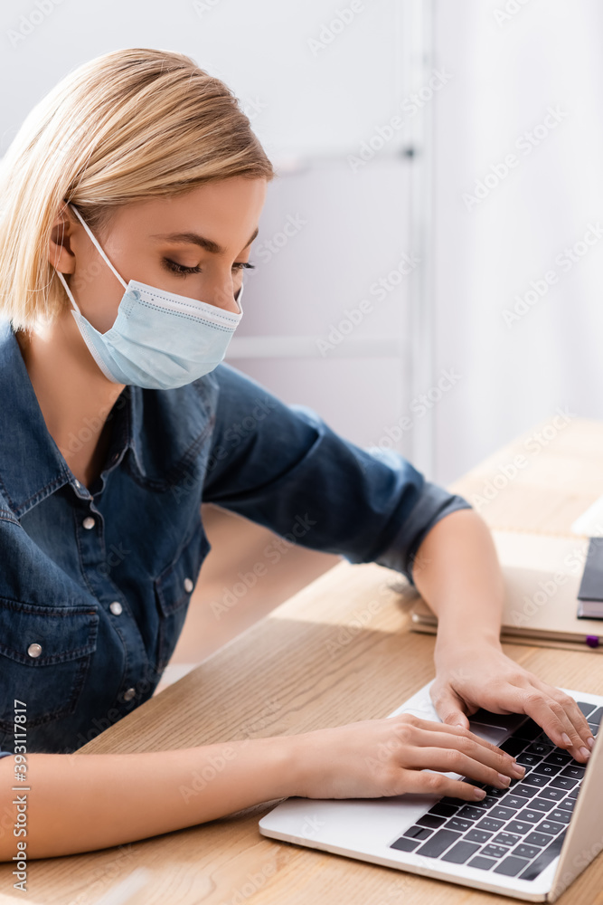young manager in medical mask typing on laptop in office young manager in medical mask typing on laptop in office