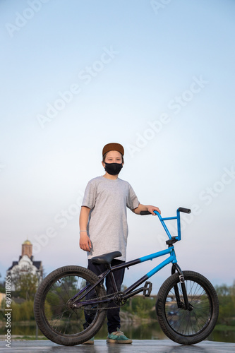 Portrait of a teenager in the sunset in a black mask on a blue bicycle. Quarantine. It is forbidden to ride a bicycle. Covid-19.