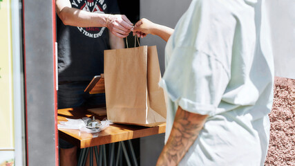 Cropped shot of woman taking paper bag with her order from hands of shop assistant while collecting her purchase from the pickup point