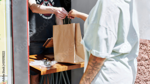 Cropped shot of woman taking paper bag with her order from hands of shop assistant while collecting her purchase from the pickup point
