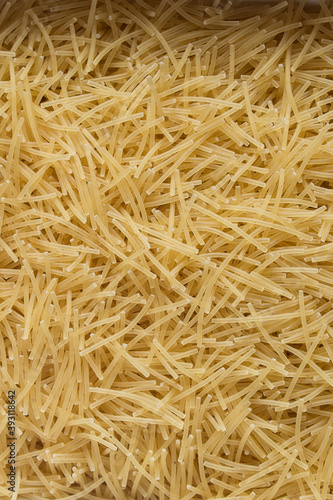 Vertical close-up of a plate full of raw noodle pasta with traces of egg. . Organic textures as a background. Vegan food.