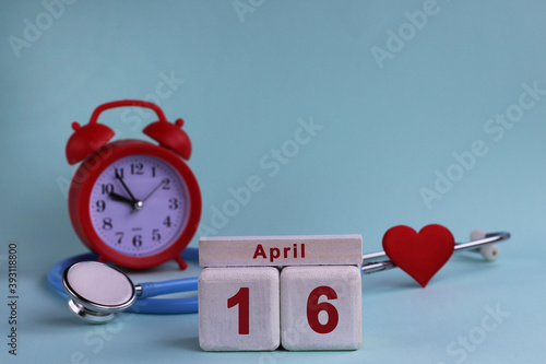 April 16st. White wooden calendar blocks with date, clock and stethoscope on a blue pastel background. Selective focus. health concept photo