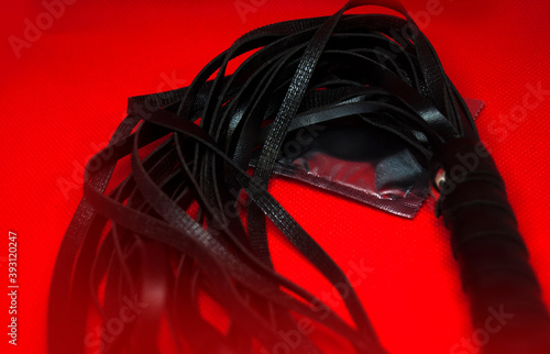 Whip / lash and condom on red background.  Submission and Domination BDSM Sex Toy Concept © A_sm