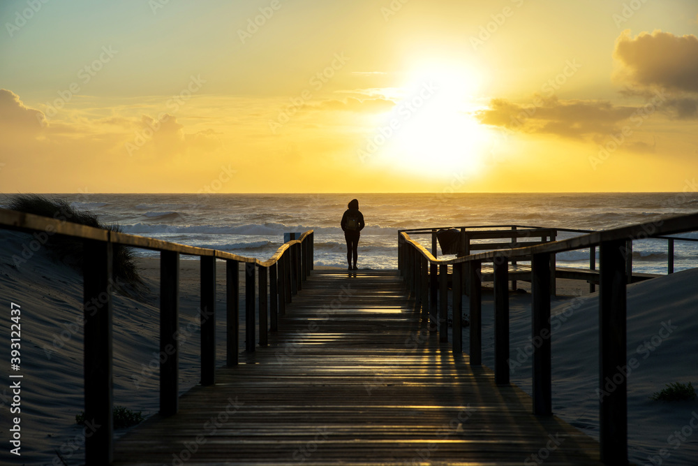 Fototapeta premium Silhouette of a woman on a wooden path looking out to sea during a sunset