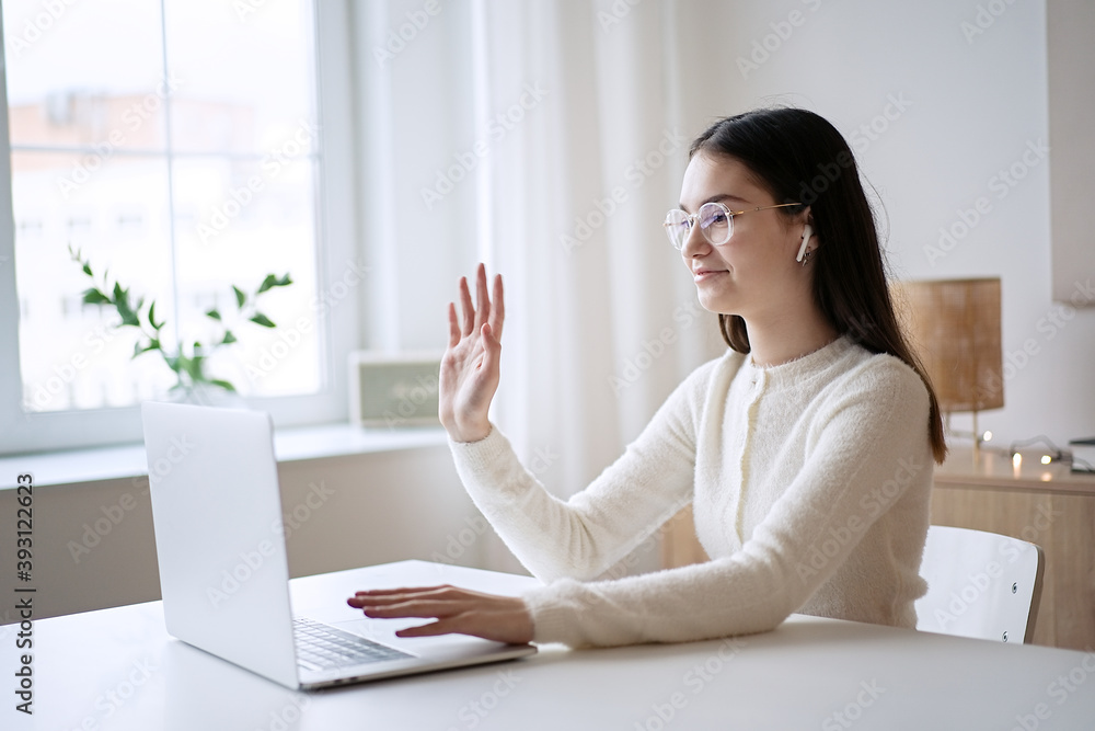 Cute teenage girl waving hand with online teacher on laptop screen at home. Education concept, distance learning, self-education, video conference class with tutor Cute teenage girl waving hand with online teacher on laptop screen at home. Education concept, distance learning, self-education, video conference class with tutor