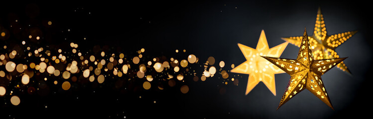Ornamental gold star lanterns for Christmas on black background with golden bokeh stardust, extra wide format 