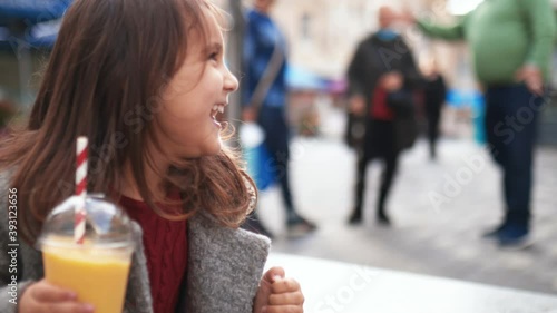 Happy little girl holding a yellow smoothie and making funny faces