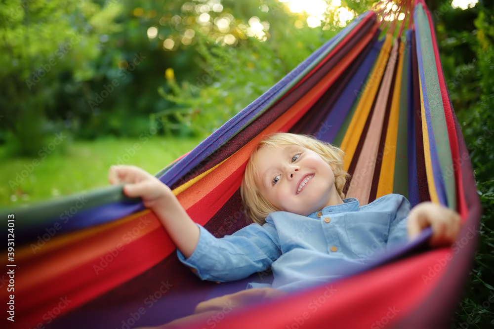 Cute little blond caucasian boy enjoy and having fun with multicolored hammock in backyard or outdoor playground. Summer active leisure for kids. Child swinging and relaxing in hammock. Cute little blond caucasian boy enjoy and having fun with multicolored hammock in backyard or outdoor playground. Summer active leisure for kids. Child swinging and relaxing in hammock.