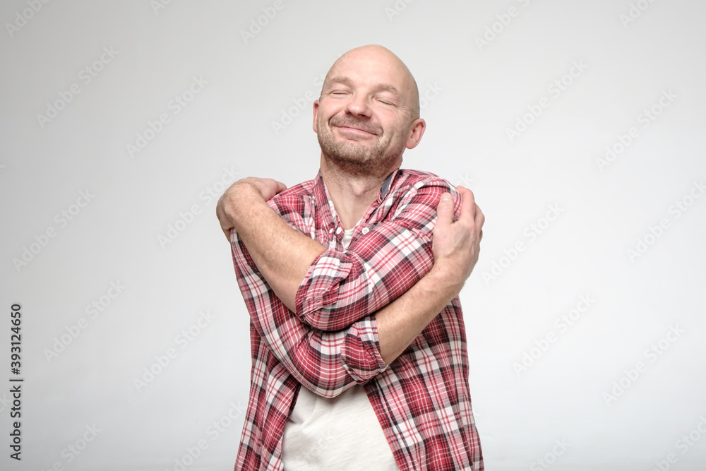Handsome man in a plaid shirt hugs himself and dreams with his eyes closed. If you feel lonely, hug yourself. Handsome man in a plaid shirt hugs himself and dreams with his eyes closed. If you feel lonely, hug yourself.