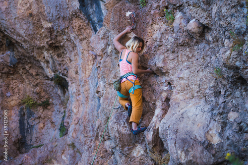A strong woman climbs a beautiful orange rock.