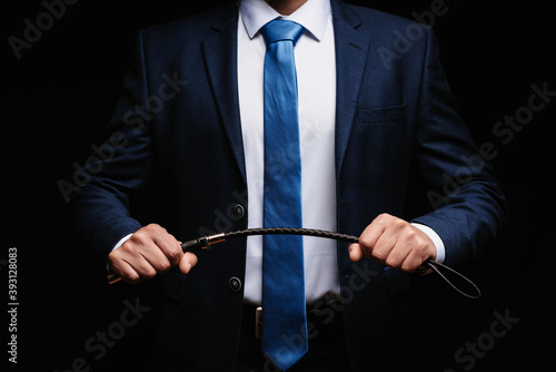 Male dominant businessman in a suit holding a leather whip Flogger for domination