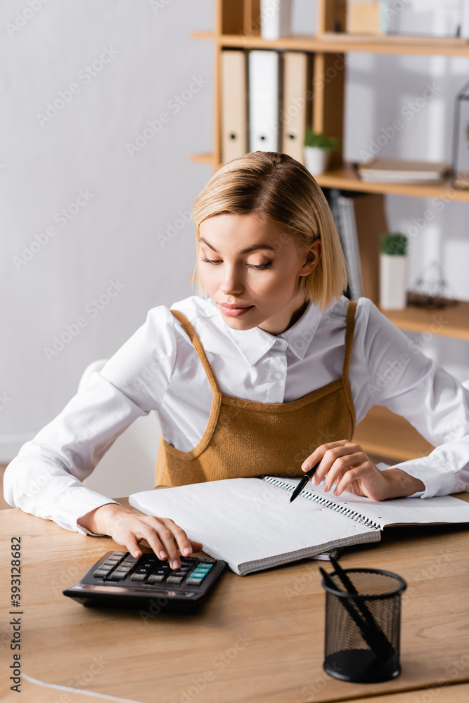 young, focused accountant working with calculator near blank notebook young, focused accountant working with calculator near blank notebook