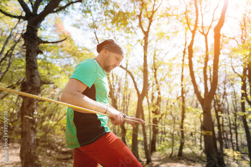 Portrait of a bearded man in age stands near a taut slackline in an autumn forest photo