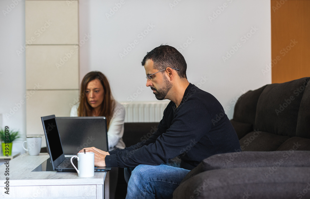 Young couple working from home sitting on the couch with their laptops Young couple working from home sitting on the couch with their laptops