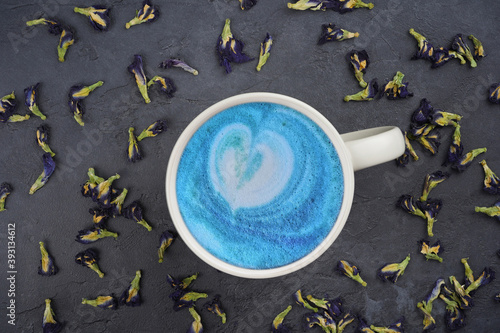 Blue tea latte in cup with heart shape, dried butterfly pea flowers pattern on gray concrete background. Menu, recipe, beverage concept. Flat lay, top view
