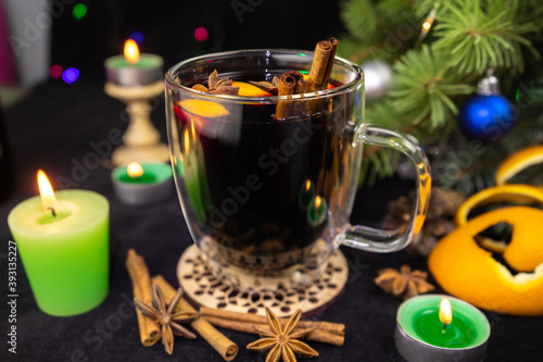 Hot mulled wine with red wine, orange, cinnamon sticks and star anise. Cosy Christmas decoration with candles on black background