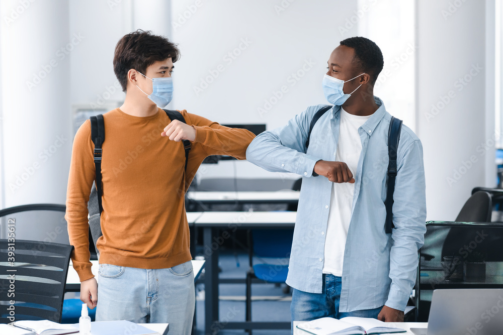 Obraz premium Multiracial students wearing face masks greeting and bumping elbows