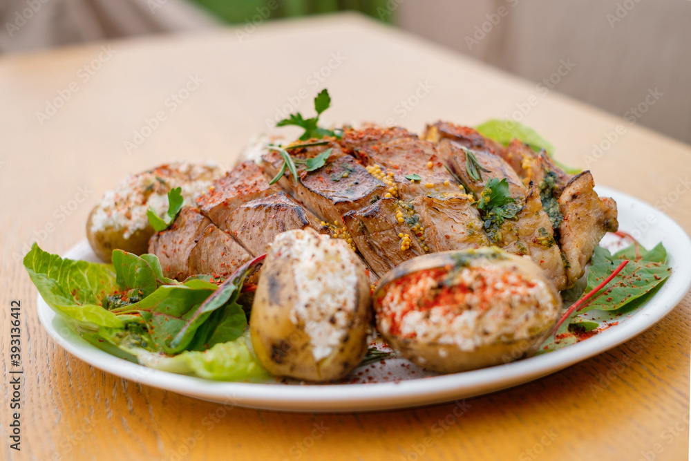 Defocused blurred baked meat with potatoes decorated with spices and herbs on a white plate close-up. Defocused blurred baked meat with potatoes decorated with spices and herbs on a white plate close-up.