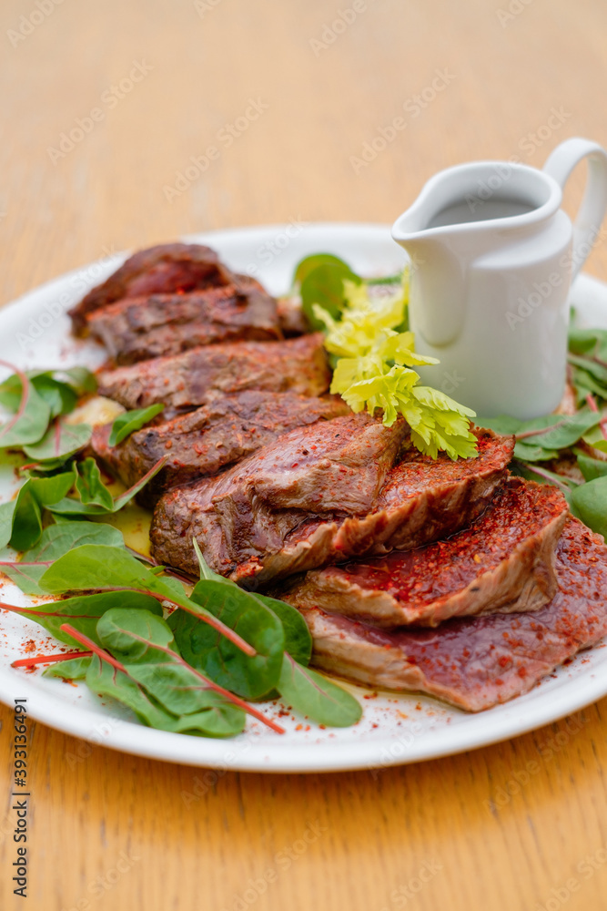 Rare meat steak with spices and sauce garnished with greens side view.