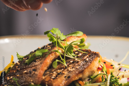 Pan fried sea-pass fillets served on a base of Asian vegetables, garnished with viola flowers and sesame seeds.