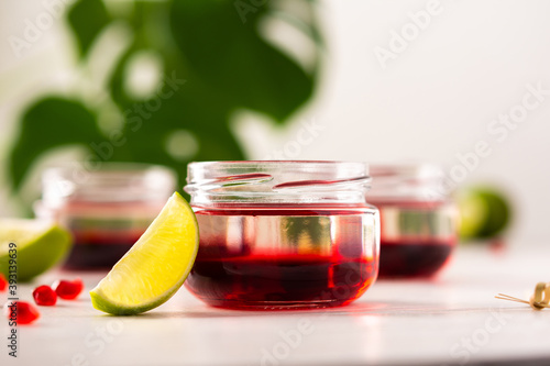 Red alcoholic shots on white background , small jars with liquor and grenadine with lime