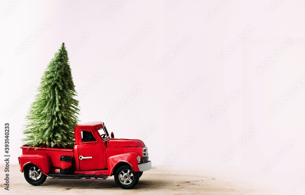 Little red toy car with green Christmas tree on the white background. Christmas preparations. Side view. Copyspace