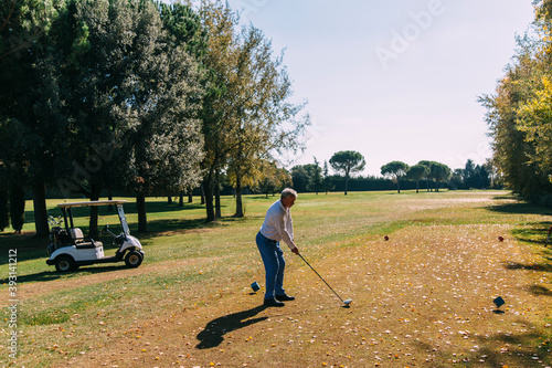 Senior golfer lining up shot with iron club on golf course in autumn