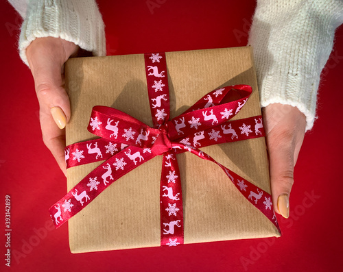 Female hands with Christmas gift with red ribbon. Top view on red background.