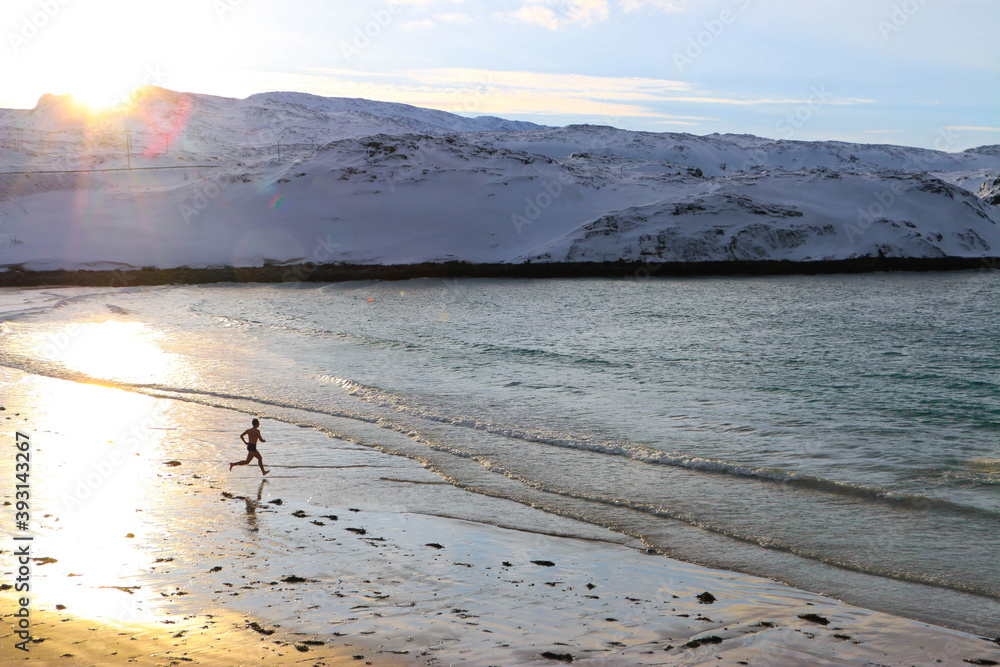 IMAGE OF A PERSON RUNNING TO THE SEA AT NORWAY. PERSON GOING INTO THE COLD WATER OF THE SCANDINAVIAN SEA. COLD, SNOW AND SUNSET CONCEPT IMAGE OF A PERSON RUNNING TO THE SEA AT NORWAY. PERSON GOING INTO THE COLD WATER OF THE SCANDINAVIAN SEA. COLD, SNOW AND SUNSET CONCEPT