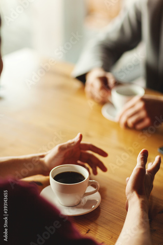 Hands of two unrecognizable businessmen having business talk over coffee sitting at table in cafe