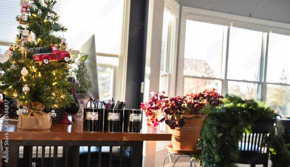 Fototapeta premium Multitasking while telecommuting. Computer sitting on a cherry stand up desk with Christmas tree on a sunny day with giant pot of shamrocks in background and a large wreath awaiting decoration.