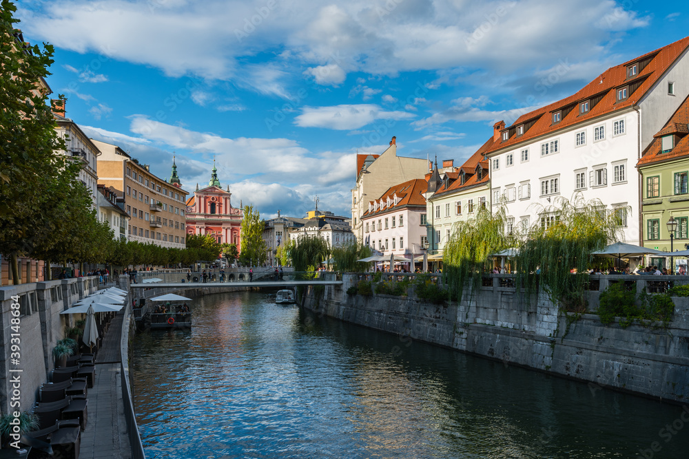 The promenade on the Ljubljanica river in the slovenian capital city Ljubljana with the Triple bridge, Ribja bridge and famous pink franciscan church on sunny day in summer with clouds