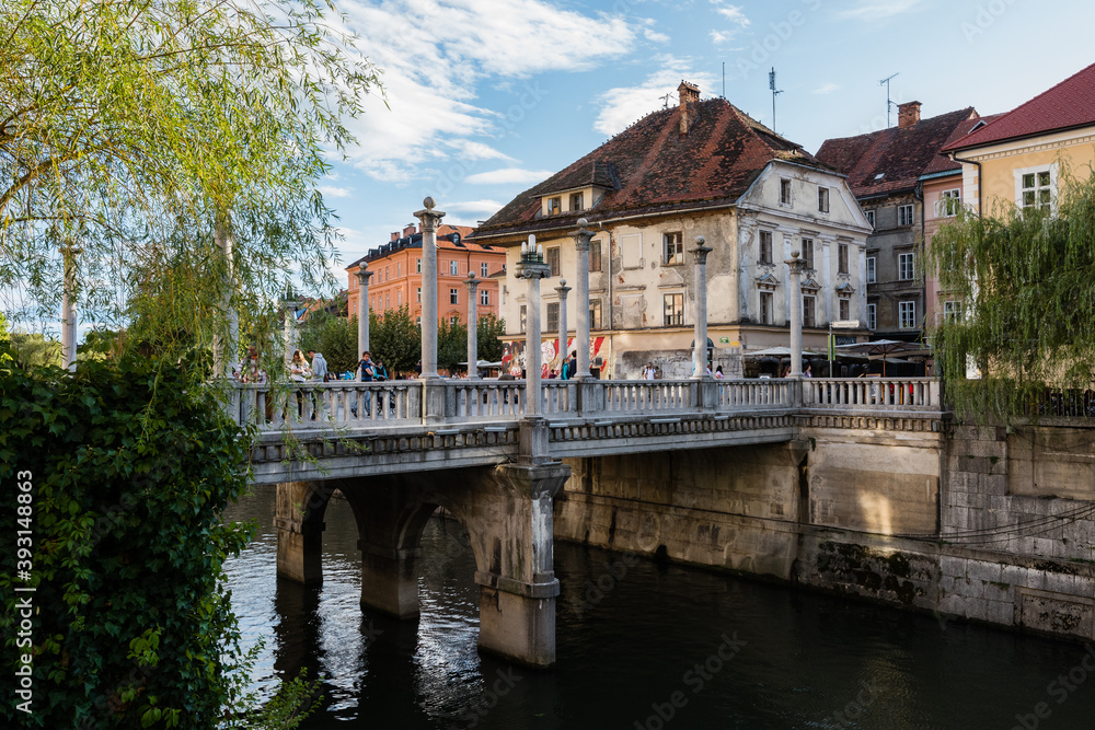 The iconic Cobblers bridge in Ljubljana with Ljubljanica river and old house in background on sunny day