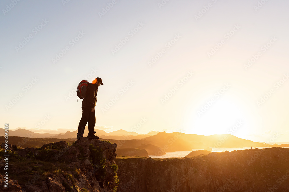 Side view of anonymous male hiker with backpack standing on rock in mountains and enjoying amazing sundown during vacation Side view of anonymous male hiker with backpack standing on rock in mountains and enjoying amazing sundown during vacation
