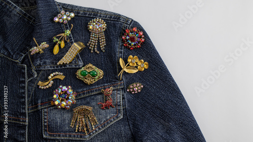 Foto A variety of beautiful multi colored vintage brooches are  pinned on a dark blue denim jacket