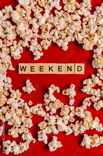  The word" weekend " from wooden blocks lies on a red background surrounded by popcorn. The concept of recreation with watching movies