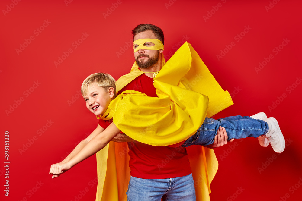 Obraz premium dad and kid boy play superhero game, imitate flight isolated over red studio background, dream to be superhero, entertainment