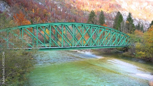 Elevated view of Alpine river flowing under iron railway bridge. Passenger train passing by. Beautiful and colorful autumn season in Slovenia. Wide angle, static shot, real time photo