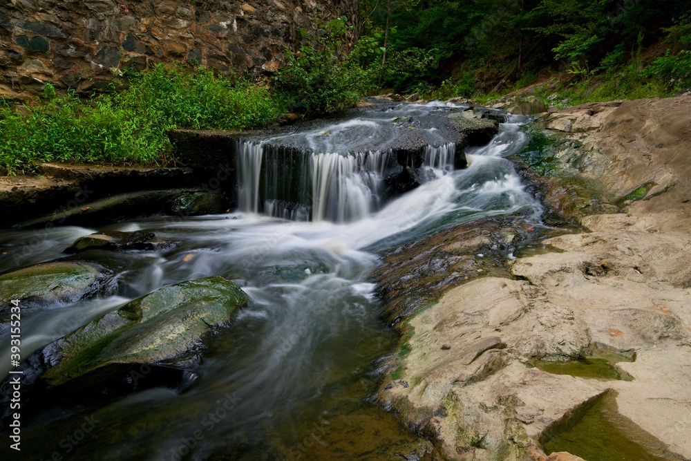 Small waterfall pouring over rocky cascades next to forest Small waterfall pouring over rocky cascades next to forest